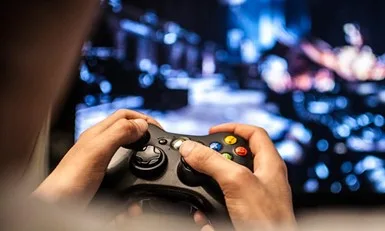 Close-up of a person's hands holding a game controller in front of a blurred, glowing television screen