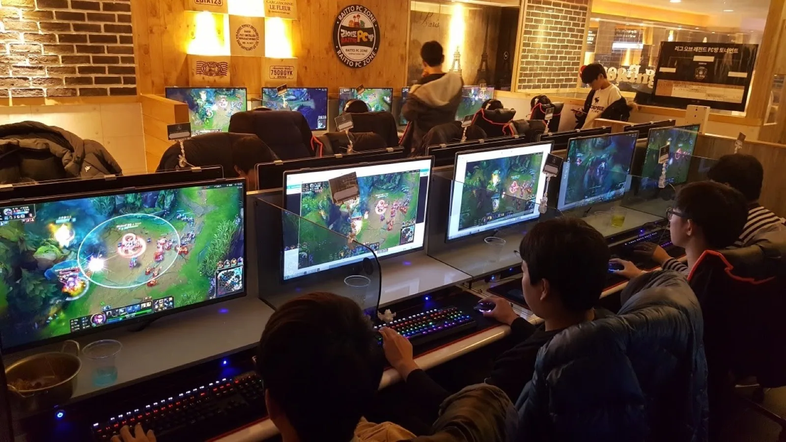 Players at rows of computers in a Korean PC cafe, with League of Legends matches on their screens