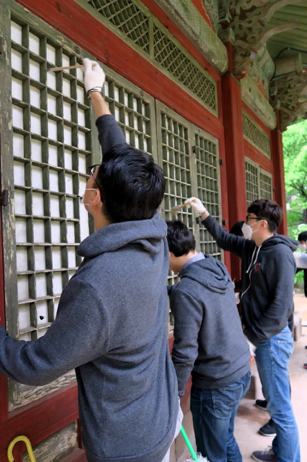 Riot volunteers in gloves and masks cleaning the red-framed lattice doors of a historic Korean building