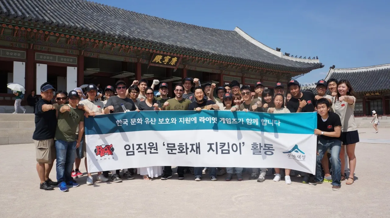 Riot Games employees raising fists behind a Korean banner reading 'Cultural Heritage Guardians' in front of a traditional palace hall